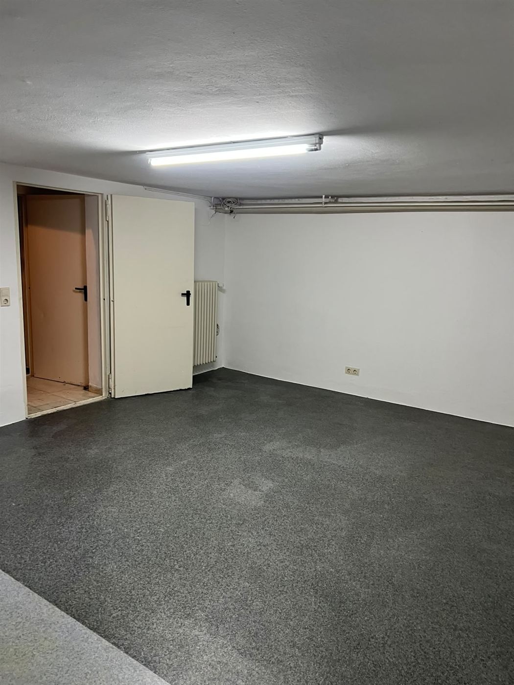 Renovierter Kellerraum mit weißen Wänden, grauem Boden und Heizkörper